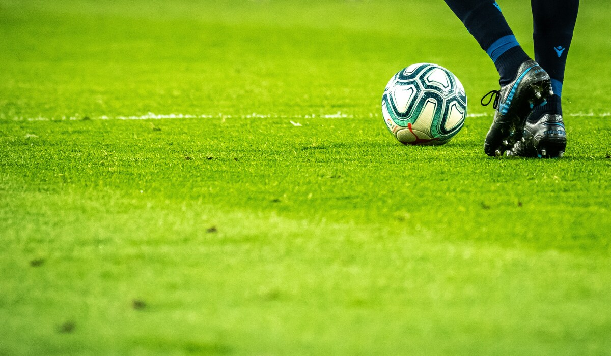 Fußball und Beine mit schwarzen Schuhen und Stutzen auf grünem Rasen