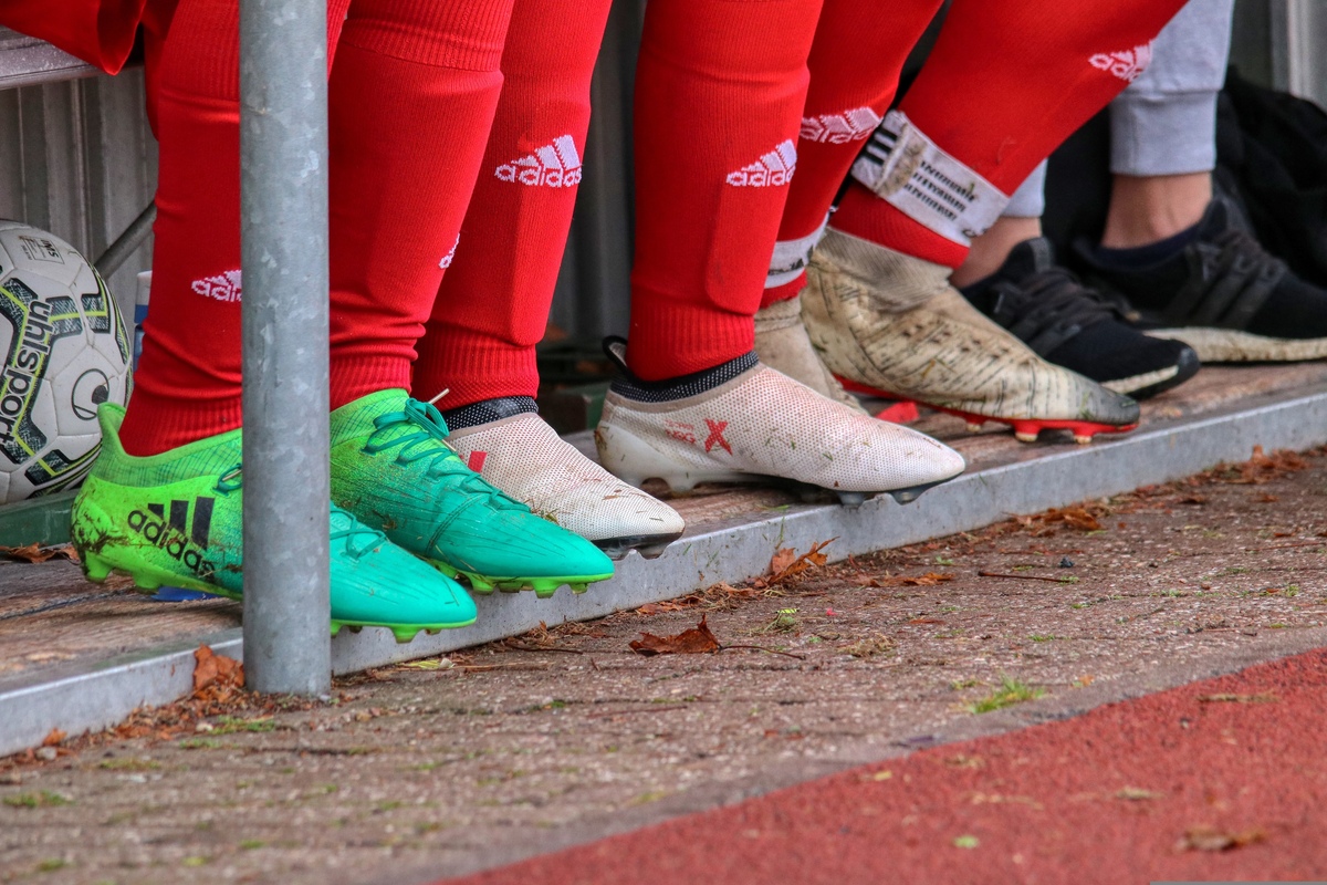 Fu&szlig;ballschuhe auf Ersatzbank, alle mit roten Stutzen