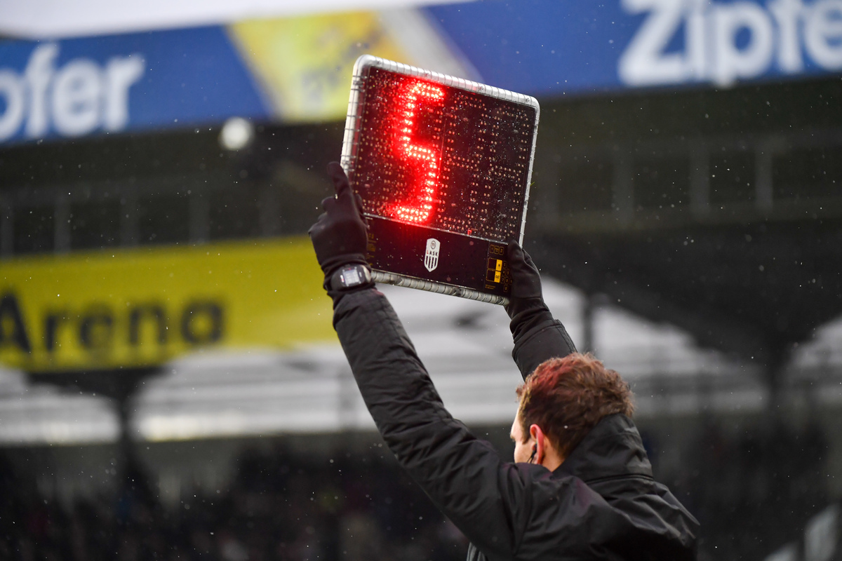 Mann hält Anzeigetafel, die eine Nachspielzeit von fünf Minuten anzeigt