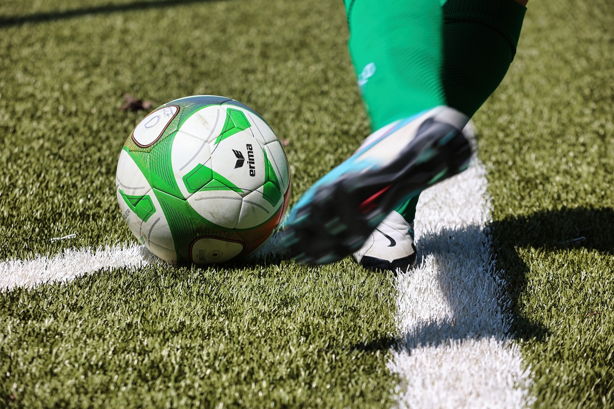 Nahaufnahme: Spieler holt zum Eckball aus. Weiß-grüner Ball, grüne Stutzen